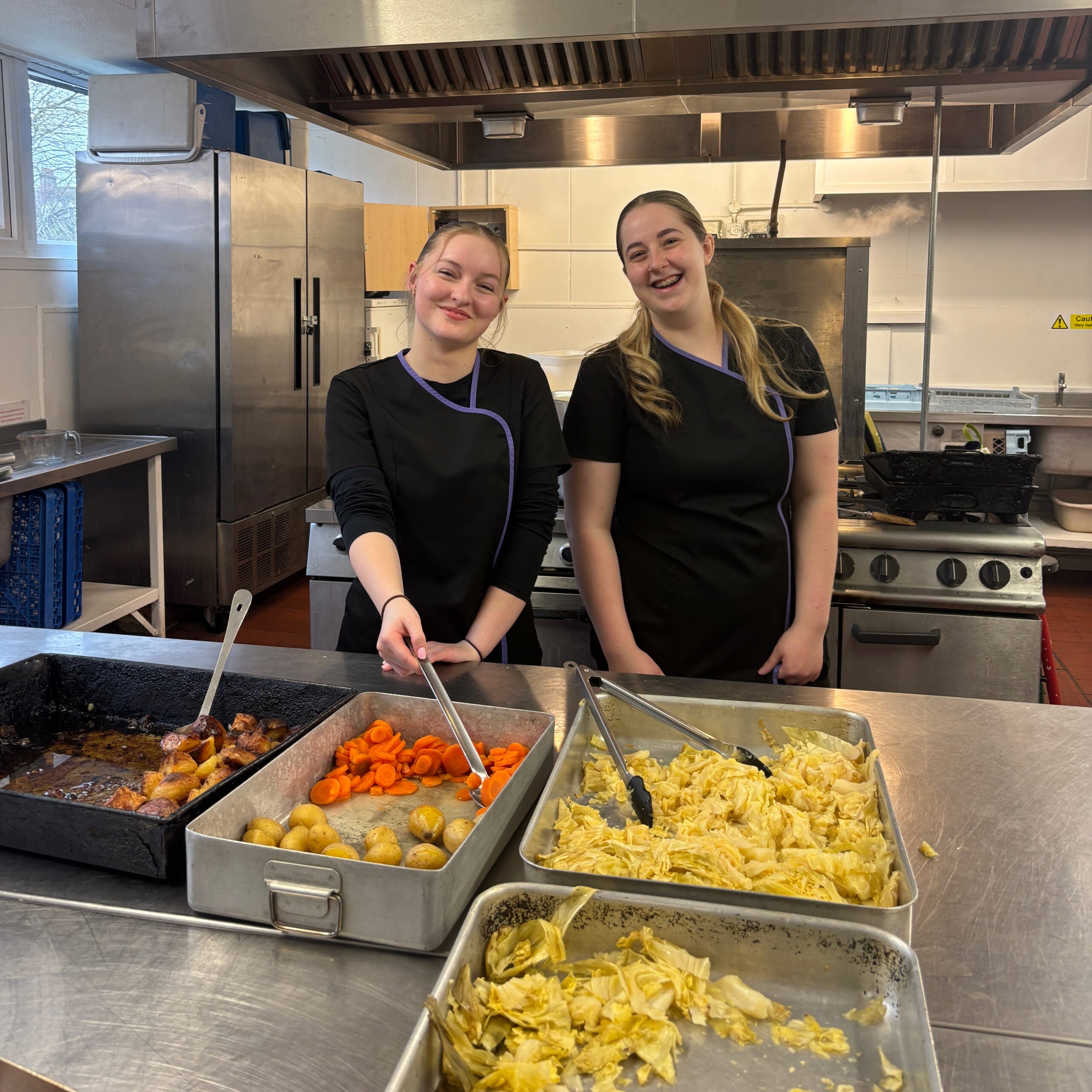 Two students volunteering at a care home serving hot meals 