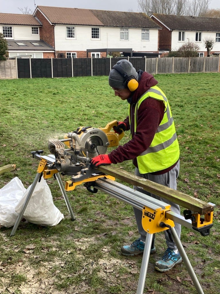 Student using an electric saw to cut fence post 