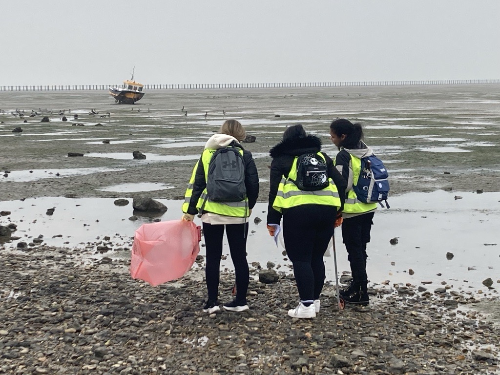 Three students litter picking at a beach in Southend