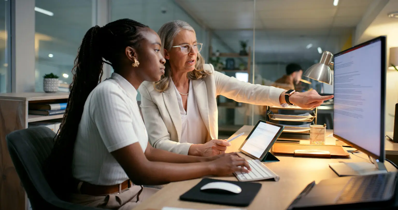 Woman showing girl computer screen in office