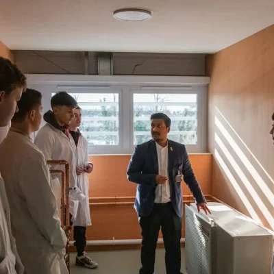 4 males students in lab coats being taught by male teacher next to air conditioning unit