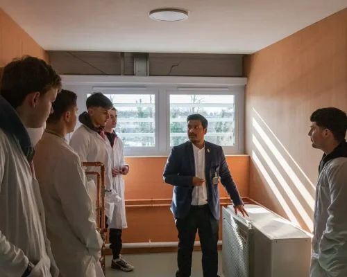4 males students in lab coats being taught by male teacher next to air conditioning unit